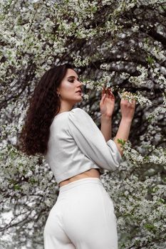 Girl touches and sniffs a branch of a white flowering tree without medical mask. Spring walking in the park