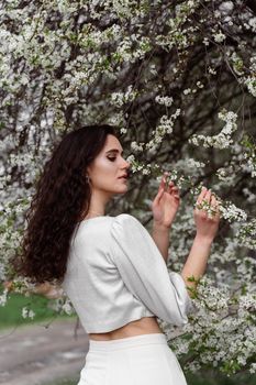 Girl touches and sniffs a branch of a white flowering tree without medical mask. Spring walking in the park