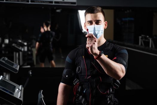 Man in EMS suit and medical mask in gym. Protection from coronavirus covid-19. Sport training in electrical muscle stimulation suit at quarantine period