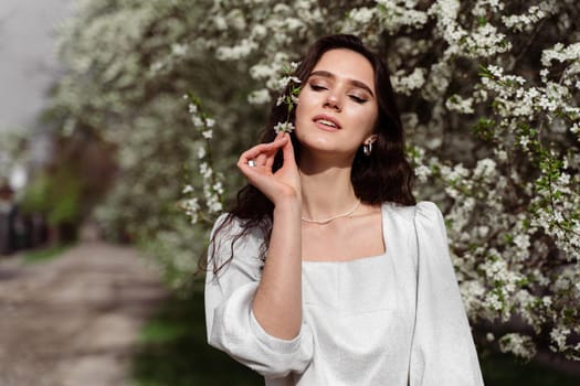 Lovely girl near blooming trees in the park. Outdoor walking in at sunny day. Lifestyle of young woman