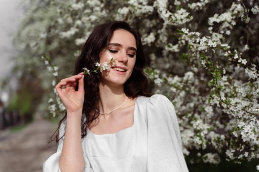 Lovely girl near blooming trees in the park. Outdoor walking in at sunny day. Lifestyle of young woman