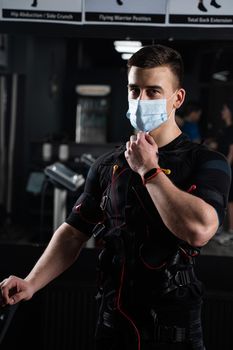 Man in EMS suit and medical mask in gym. Protection from coronavirus covid-19. Sport training in electrical muscle stimulation suit at quarantine period