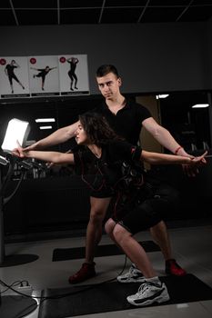 Man trainer trains a girl in an EMS suit in the gym. Electrical stimulation of the misc during active training.