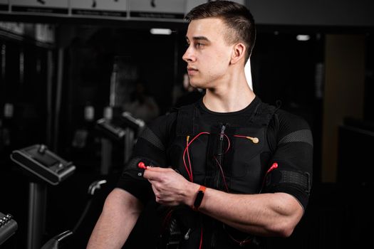 Handsome trainer in EMS suit with red wires for electro impulse stimulation for body. Training in gym