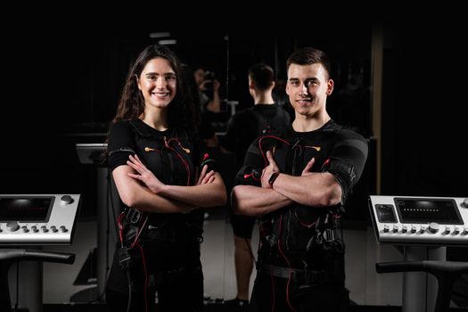 man and a woman in an EMS vest are standing side by side and smiling. 2 trainers in gym.