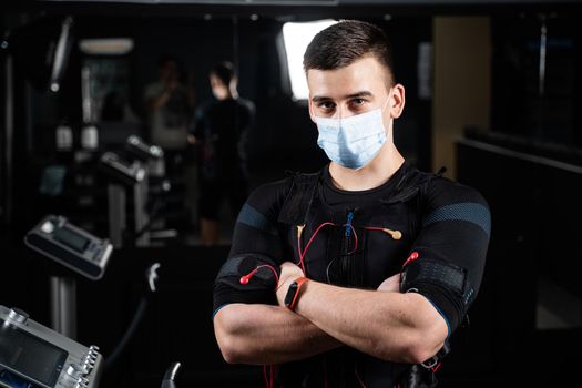 Man in EMS suit and medical mask in gym. Protection from coronavirus covid-19. Sport training in electrical muscle stimulation suit at quarantine period