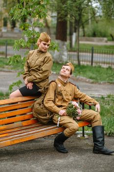 A girl and a soldier in a Soviet military uniform. The military sit on a wooden bench, looking at each other