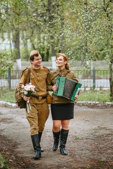 A soldier walks down the alley, hugging a military girl playing an accordion, spring, people returned from the war