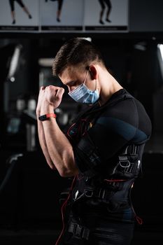 Man in EMS suit and medical mask in gym. Protection from coronavirus covid-19. Sport training in electrical muscle stimulation suit at quarantine period