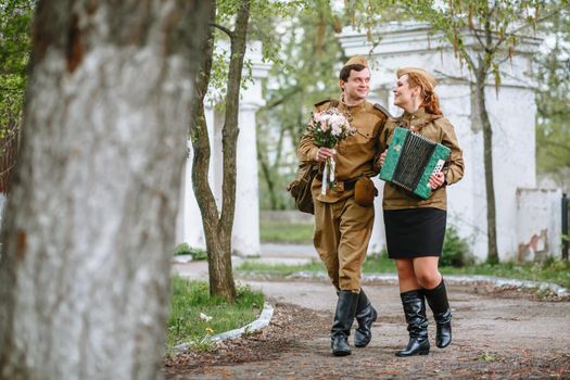 A soldier walks down the alley, hugging a military girl playing an accordion, spring, people returned from the war