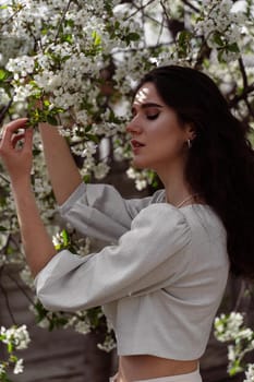 Lovely girl near blooming trees in the park. Outdoor walking in at sunny day. Lifestyle of young woman