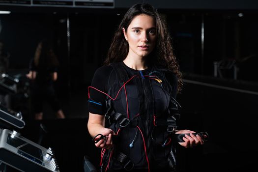 Girl in EMS suit in gym. Sport training in electrical muscle stimulation suit. Making physical exercises.