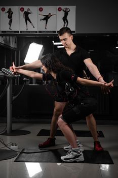 Man trainer trains a girl in an EMS suit in the gym. Electrical stimulation of the misc during active training.