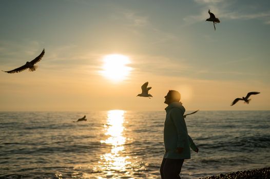 Caucasian woman feeding seagulls at sunset by the sea