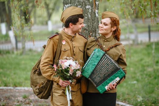 A soldier walks down the alley, hugging a military girl playing an accordion, spring, people returned from the war