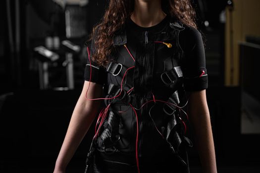 Girl in EMS suit in gym. Sport training in electrical muscle stimulation suit