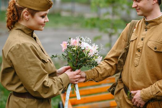 A military girl and a soldier in a Soviet military uniform. Military gives a girl a bouquet