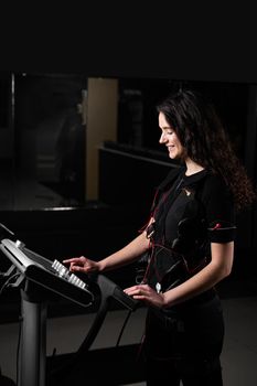 Girl in EMS suit in gym. Sport training in electrical muscle stimulation suit