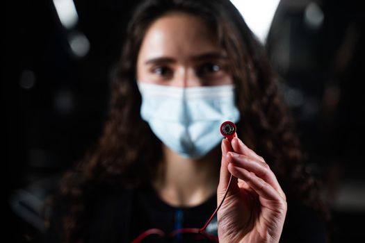 Girl in EMS suit and medical mask in gym. Protection from coronavirus covid-19. Sport training in electrical muscle stimulation suit at quarantine period