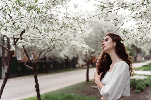 Spring lifestyle. Model posing near white blooming trees without mask outdoor countryside. Dreaming girl with curly hair