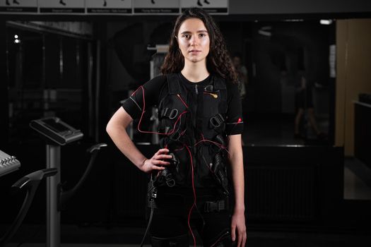 Girl in EMS suit in gym. Sport training in electrical muscle stimulation suit