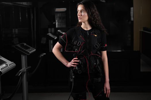 Girl in EMS suit in gym. Sport training in electrical muscle stimulation suit