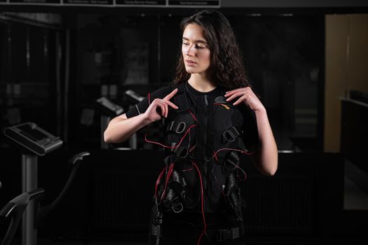 Girl in EMS suit in gym. Sport training in electrical muscle stimulation suit