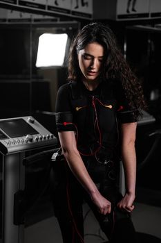 Girl in EMS suit in gym. Sport training in electrical muscle stimulation suit. Making physical exercises.