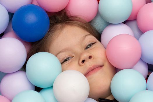 Face of caucasian little girl of 6 years among multicolor balls in play center inside