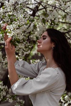 Lovely girl near blooming trees in the park. Outdoor walking in at sunny day. Lifestyle of young woman