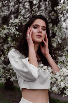 Lovely girl near blooming trees in the park. Outdoor walking in at sunny day. Lifestyle of young woman