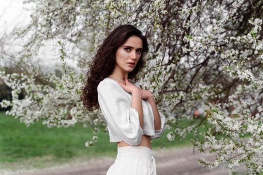 Portrait of young woman in the garden. Attractive girl weared white dress posing near blooming trees