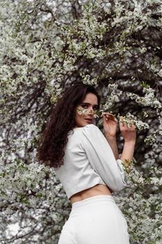 Girl touches and sniffs a branch of a white flowering tree without medical mask. Spring walking in the park