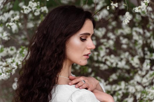 Portrait of young woman in the garden. Attractive girl weared white dress posing near blooming trees