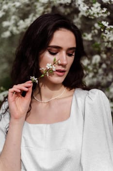 Portrait of young woman in the garden. Attractive girl weared white dress posing near blooming trees