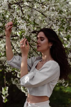 Lovely girl near blooming trees in the park. Outdoor walking in at sunny day. Lifestyle of young woman