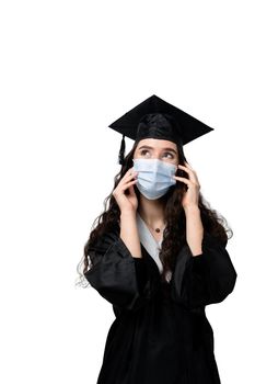 Surprised bachelor girl in medical mask at coronavirus covid-19 period. Master in graduation robe and cap on white background. Distance learning online. Study at home. Graduation from college.