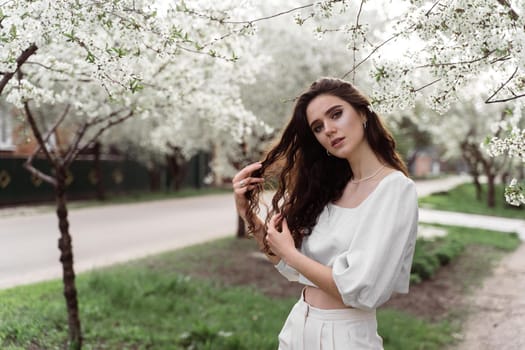 Spring lifestyle. Model posing near white blooming trees without mask outdoor countryside. Dreaming girl with curly hair