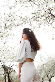 Lovely girl near blooming trees in the park. Outdoor walking in at sunny day. Lifestyle of young woman.