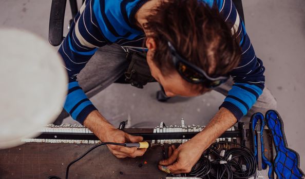 Industrial worker man soldering cables of manufacturing equipment in a factory. Selective focus. High-quality photo