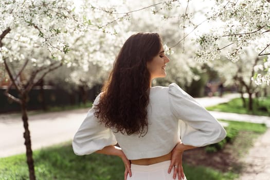 Lovely girl near blooming trees in the park. Outdoor walking in at sunny day. Lifestyle of young woman.