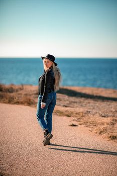 A blonde in a stylish black leather jacket walks along the seashore