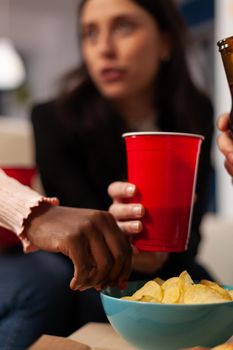 Office workers having fun with alcoholic beverage and chips at after work celebration. Colleagues enjoying beer in bottles and glasses, eating snacks and laughing together after hours. Close up.