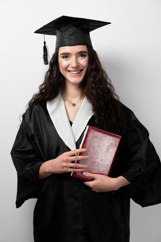 Student with book in graduation robe and cap ready to finish college. Future leader of science. Academician young woman in black gown smiling.