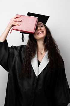 Student with book in graduation robe and cap ready to finish college. Future leader of science. Academician young woman in black gown smiling.
