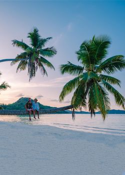 Praslin Seychelles tropical island with withe beaches and palm trees, a couple of men and a woman in with a palm tree at Anse Volber Seychelles. sunset palm tree