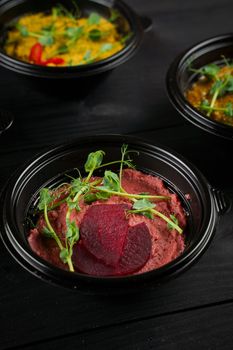 Hummus garnished peppers, chili, beet and herbs in black bowl on dark wooden table. Hummus assortment.