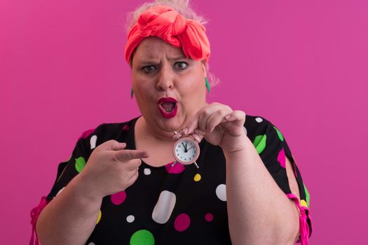 Portrait of plus size young lady smiling hands holds sand clock isolated on pink color background. High quality photo