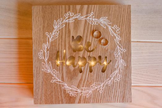 Wedding rings on a wooden background with golden inscription be happy and white pattern.