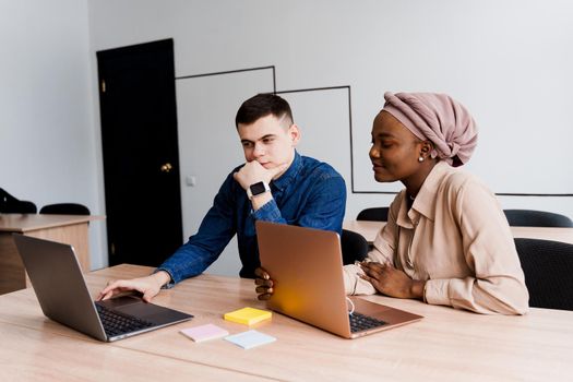 Muslim black girl and white man with laptop. Multiethnic couple work online together on business project. Working at home. Surfing internet.